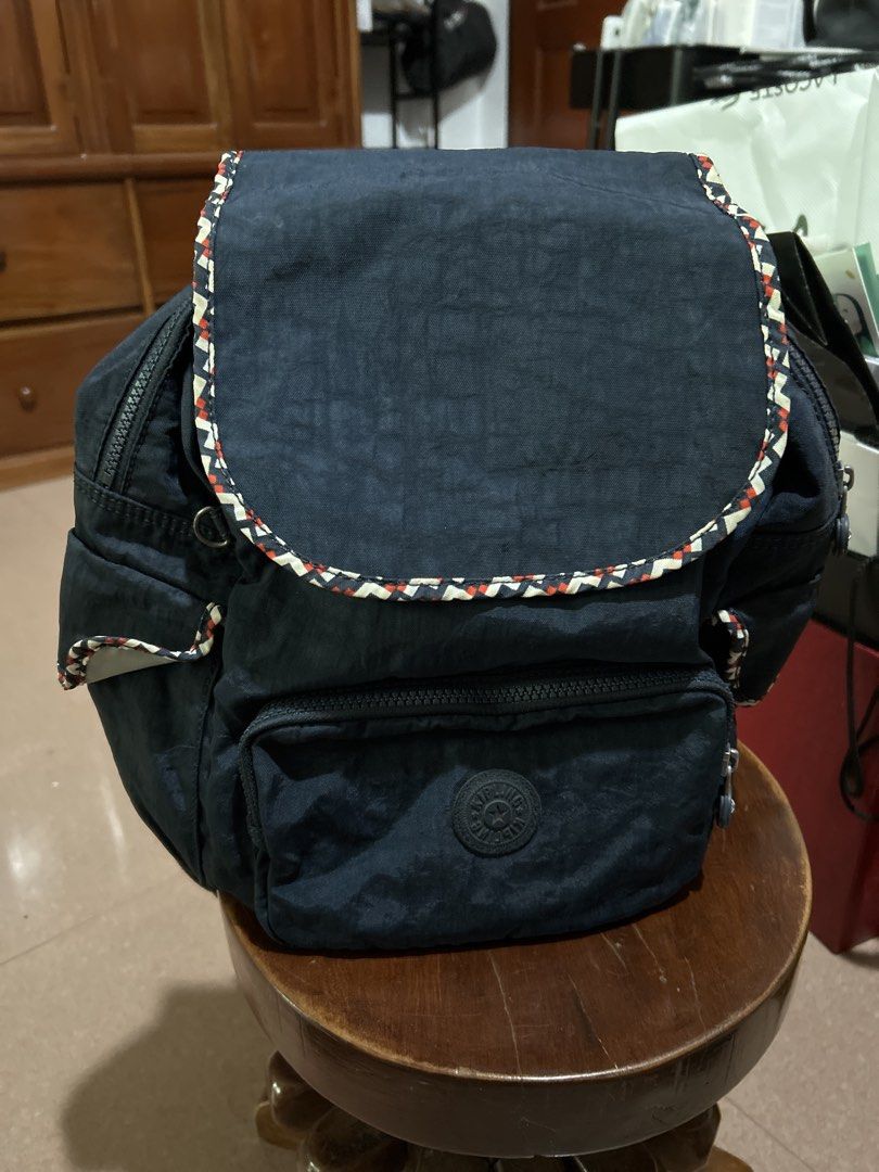 Kipling Navy Blue Backpack with Patterned Trim (Category: Backpacks) located in Alitagtag. Submitted by patrickvillanueva (Listing ID 1466623957, Image 1). Description: Navy blue nylon backpack from Kipling. Flap top with magnetic snap closure and patterned trim along the edge. Front zippered pocket with circular logo patch. Adjustable black straps on the back. Main compartment opens up with a zipper, revealing light-colored interior lining, slip