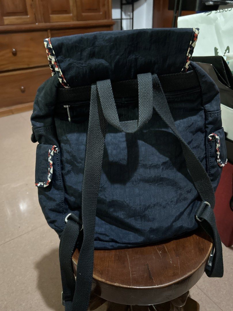Kipling Navy Blue Backpack with Patterned Trim (Category: Backpacks) located in Alitagtag. Submitted by patrickvillanueva (Listing ID 1466623957, Image 2). Description: Navy blue nylon backpack from Kipling. Flap top with magnetic snap closure and patterned trim along the edge. Front zippered pocket with circular logo patch. Adjustable black straps on the back. Main compartment opens up with a zipper, revealing light-colored interior lining, slip