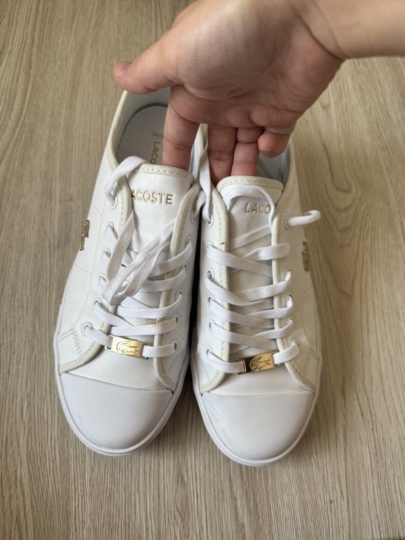 Lacoste White Leather Sneakers with Gold Hardware (Category: Sneakers) located in Rodriguez. Submitted by sheddmycloset (Listing ID 1466712363, Image 2). Description: - Authentic white leather Lacoste sneakers - Elegant gold hardware including eyelets and branded lace lock plates - Classic low-top design with durable rubber toe caps - Comfortable Ortholite insoles for all-day wear - Clean white laces and soles showing minimal signs of use.