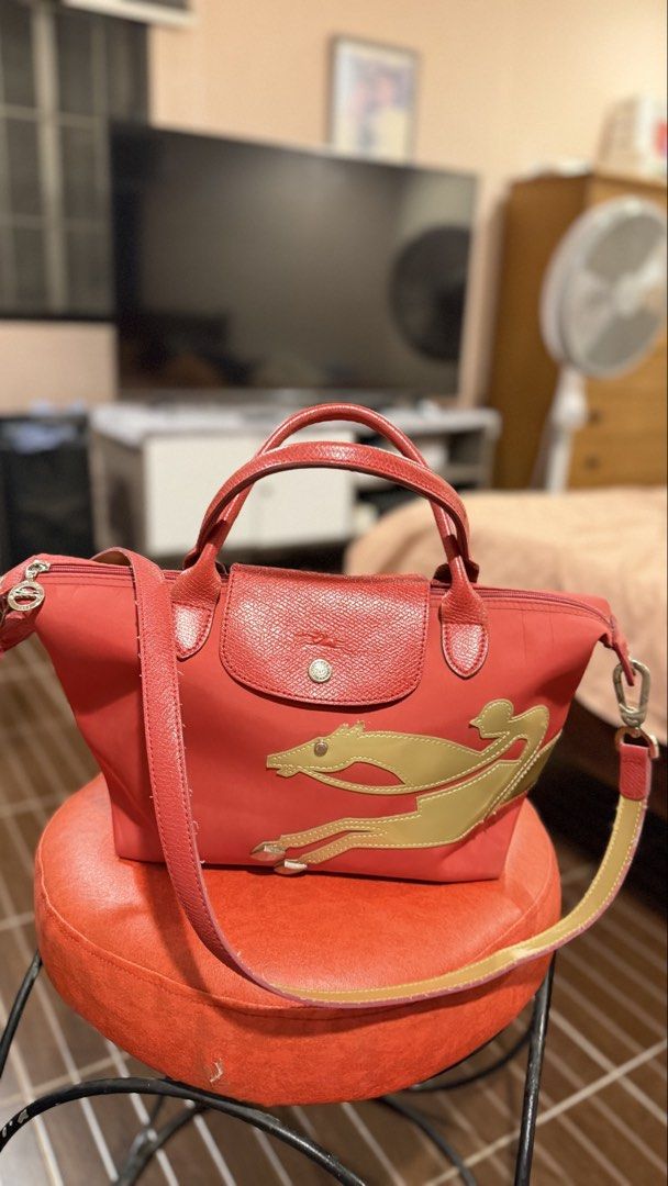 Longchamp Le Pliage Red Tote Bag with Strap (Category: Luxury Bags & Wallets) located in San Fernando. Submitted by jusaki17 (Listing ID 1466703053, Image 1). Description: - Brand: Longchamp - Color: Red with leather trim and gold-tone hardware - Material: Durable nylon - Features: Top handles, detachable shoulder strap, zip-top closure with snap flap, and iconic gold horse appliqué - Interior: Roomy main compartment with matching printed fabric 