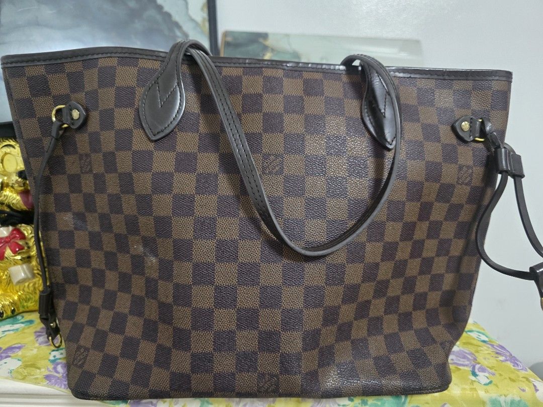 Louis Vuitton Damier Ebene Neverfull Tote Bag (Category: Luxury Bags & Wallets) located in Binan City. Submitted by geraldinef58404 (Listing ID 1466617874, Image 2). Description: Louis Vuitton Neverfull tote bag in the classic Damier Ebene canvas print. Brown and dark brown checkered pattern with dark brown leather shoulder straps and side cinch laces. Gold-tone hardware throughout. Red interior lining inside. Roomy everyday shoulder bag with sli