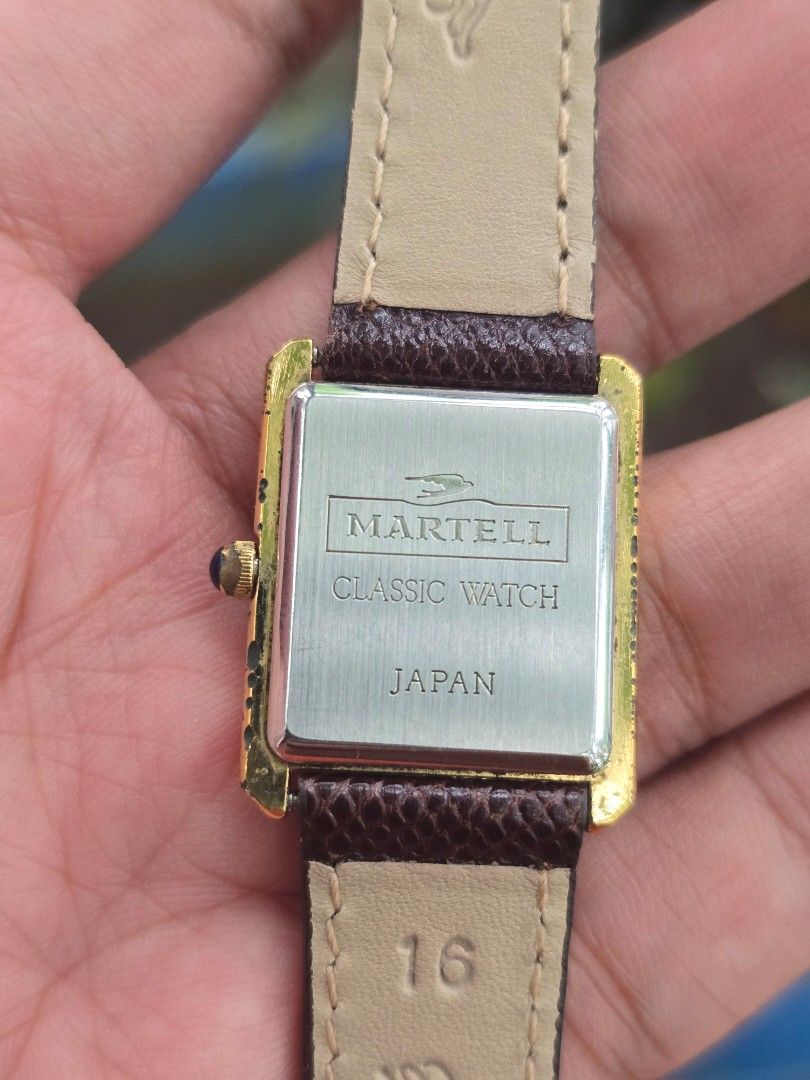 Martell Classic Watch Rectangular Tank Roman Numerals (Category: Luxury Watches) located in Manila. Submitted by timearcph (Listing ID 1466608645, Image 2). Description: - Brand/Model: Martell classic rectangular watch - Dial: White with black Roman numerals and slender black hands - Case: Gold-tone with a stylish blue cabochon crown (shows minor wear on edges) - Strap: Dark brown textured leather with contrast stitching (16mm width) - Movement: 