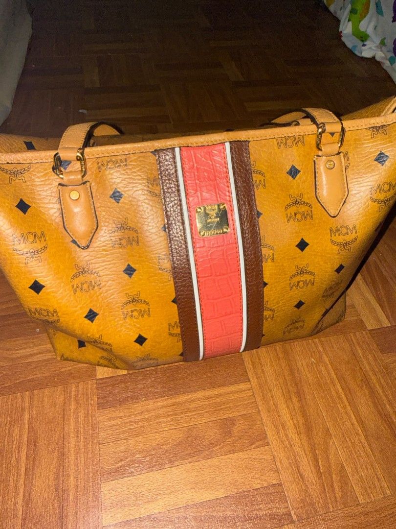 MCM Monogram Tote Bag with Center Stripe (Category: Luxury Bags & Wallets) located in Quezon City. Submitted by prelovedco (Listing ID 1466679845, Image 3). Description: - Brand: MCM Monogram Tote Bag - Color: Classic cognac yellow with a bold brown and pink vertical center stripe - Material: Clean coated canvas with all-over monogram print - Hardware: Premium gold-tone hardware - Straps: Comfortable dual shoulder straps - Compartments: Large ope