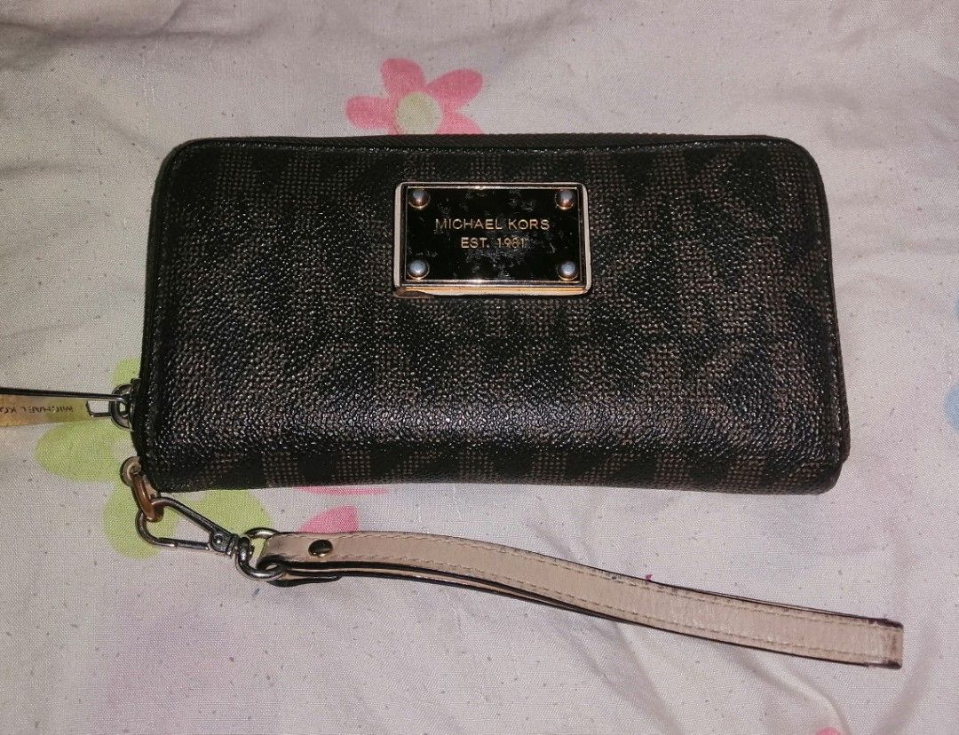 Michael Kors Brown Monogram Zip Around Wristlet Wallet (Category: Wallets & Card holders) located in Quezon City. Submitted by rolenalma (Listing ID 1466609046, Image 1). Description: Michael Kors zip-around wallet in dark brown monogram print. Includes a detachable light beige wrist strap and gold-tone hardware with an engraved plaque on the front. Interior features multiple card slots, a central zipped compartment for coins, and slip pockets fo