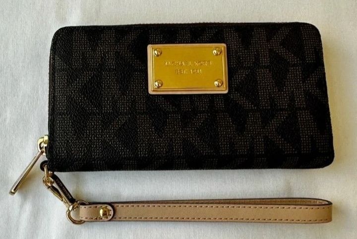 Michael Kors Brown Monogram Zip Around Wristlet Wallet (Category: Wallets & Card holders) located in Quezon City. Submitted by rolenalma (Listing ID 1466609046, Image 2). Description: Michael Kors zip-around wallet in dark brown monogram print. Includes a detachable light beige wrist strap and gold-tone hardware with an engraved plaque on the front. Interior features multiple card slots, a central zipped compartment for coins, and slip pockets fo
