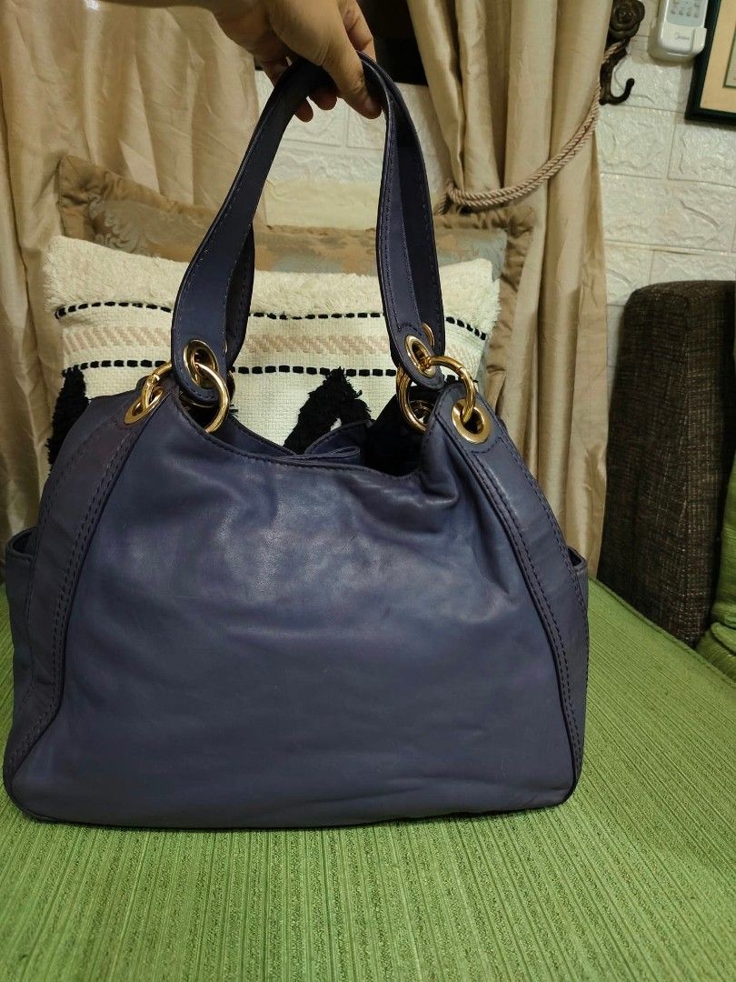 Michael Kors Purple Leather Shoulder Bag (Category: Luxury Bags & Wallets) located in Cavite. Submitted by mahthriftshop (Listing ID 1466573325, Image 2). Description: Michael Kors leather shoulder bag in a deep purple shade. Features gold-tone hardware, a drawstring closure with a toggle, and sturdy double handles attached via rings. Interior lined with signature fabric and includes an embossed brand patch along with a Made in China tag..
