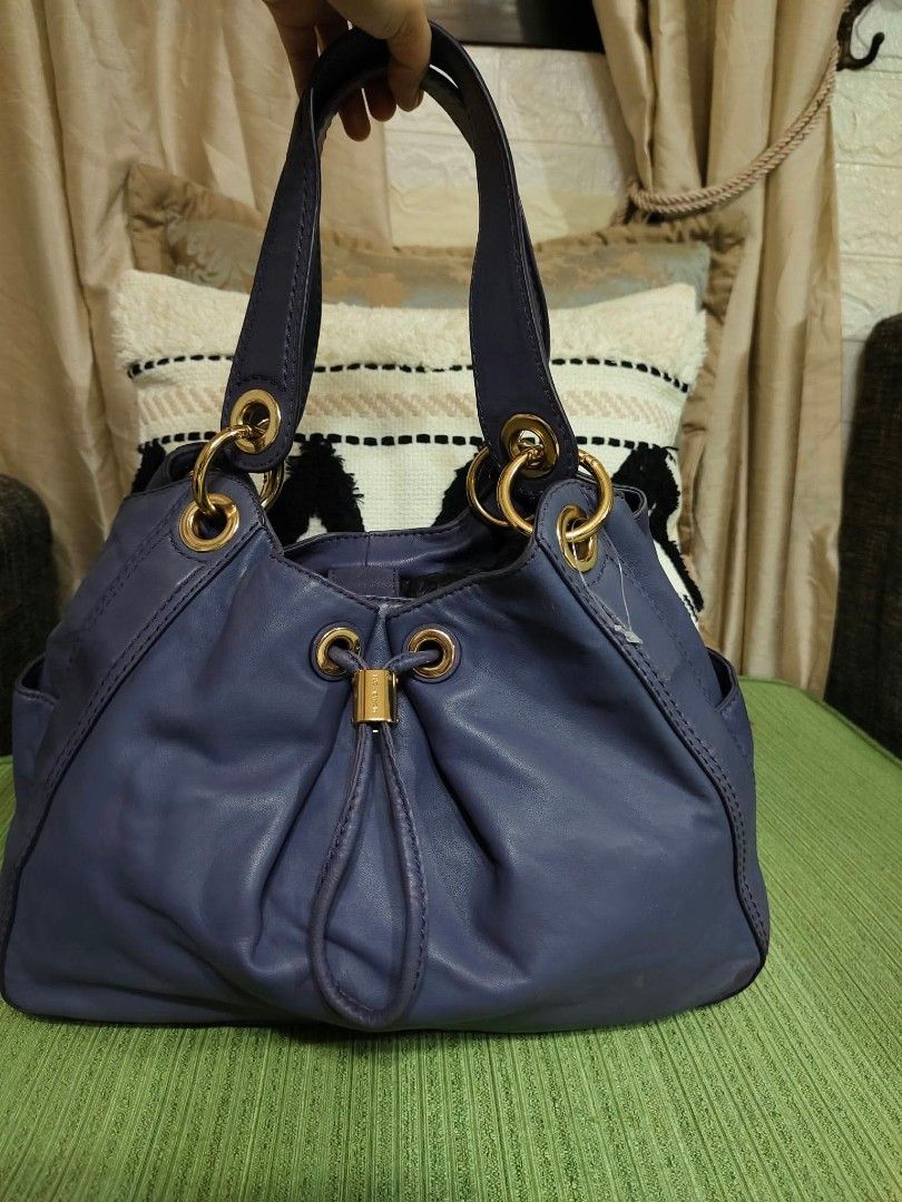 Michael Kors Purple Leather Shoulder Bag (Category: Luxury Bags & Wallets) located in Cavite. Submitted by mahthriftshop (Listing ID 1466573325, Image 1). Description: Michael Kors leather shoulder bag in a deep purple shade. Features gold-tone hardware, a drawstring closure with a toggle, and sturdy double handles attached via rings. Interior lined with signature fabric and includes an embossed brand patch along with a Made in China tag..