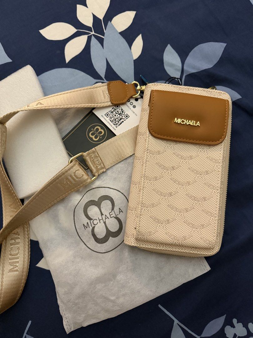 Michaela Wallet Sling Bag (Category: Cross-body Bags) located in Marikina City. Submitted by lemonlover2 (Listing ID 1466715147, Image 1). Description: - Brand: MICHAELA - Style: Crossbody bag with zip-around closure - Design: Beige monogram print with brown contrast flap pocket and gold-tone hardware - Interior: Fabric lining with zip pocket partition and protective foam insert - Strap: Adjustable thick branded webbing strap - Condition: Brand n