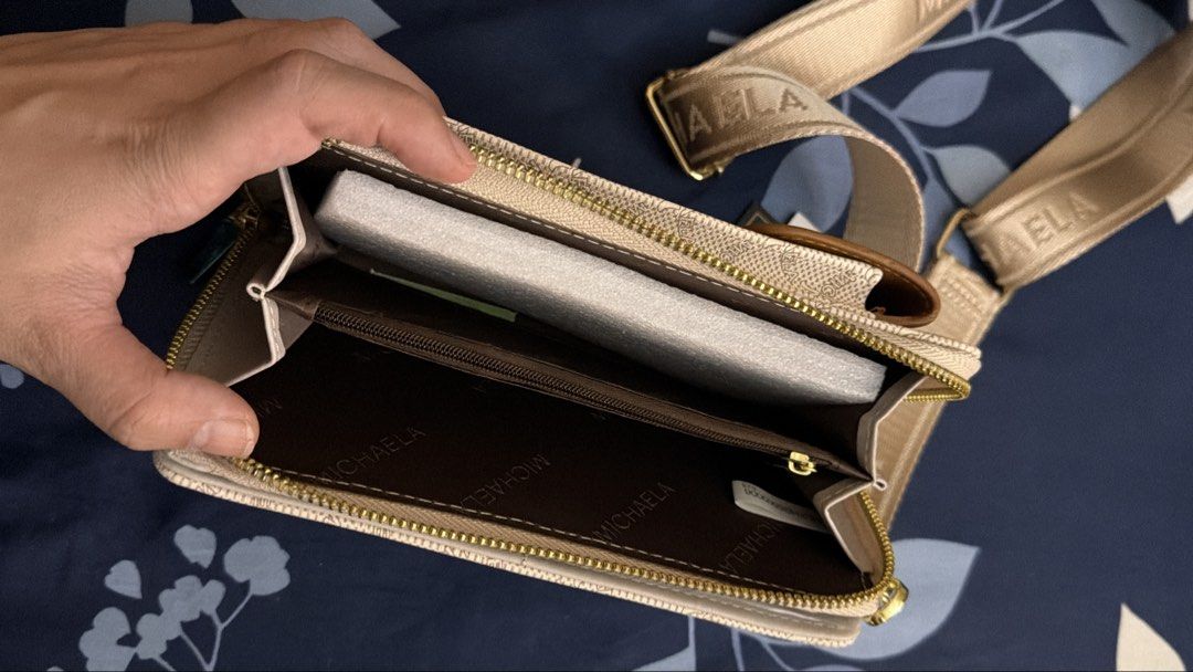 Michaela Wallet Sling Bag (Category: Cross-body Bags) located in Marikina City. Submitted by lemonlover2 (Listing ID 1466715147, Image 2). Description: - Brand: MICHAELA - Style: Crossbody bag with zip-around closure - Design: Beige monogram print with brown contrast flap pocket and gold-tone hardware - Interior: Fabric lining with zip pocket partition and protective foam insert - Strap: Adjustable thick branded webbing strap - Condition: Brand n