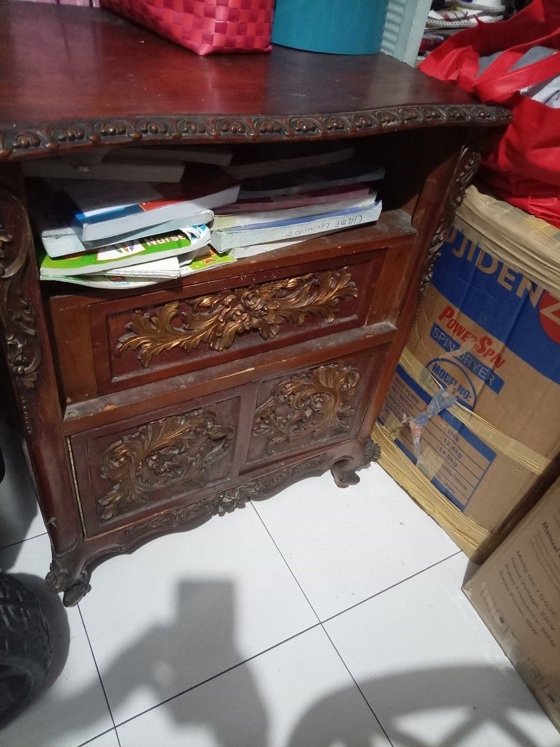 Narra for sale (Category: Shelves, Cabinets & Racks) located in Caloocan City. Submitted by maynaito (Listing ID 1466683270, Image 2). Description: - Style: Classic traditional design in rich dark wood with gold-toned carving accents - Storage: 1 pull-out drawer, lower cabinet with doors, and a handy open shelf for books - Design details: Ornate carved floral motifs, elegant scalloped top edge, and graceful cabriole legs - Condition: Solid and st