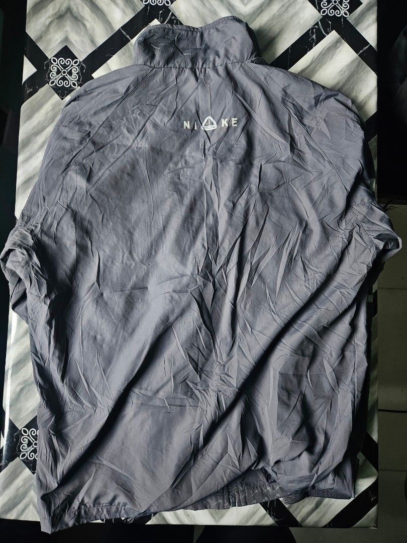 Nike ACG Grey Full Zip Windbreaker Track Jacket (Category: Coats, Jackets and Outerwear) located in Manila. Submitted by shanshan.river (Listing ID 1466593430, Image 2). Description: - Color: Grey - Brand: Nike ACG - Design: All-over subtle mini swoosh pattern - Closure: Full front zipper with standing collar - Details: Striped ribbed cuffs and hem, small ACG mountain logo and Nike lettering on the back, yellow and black woven sleeve tag - Materi