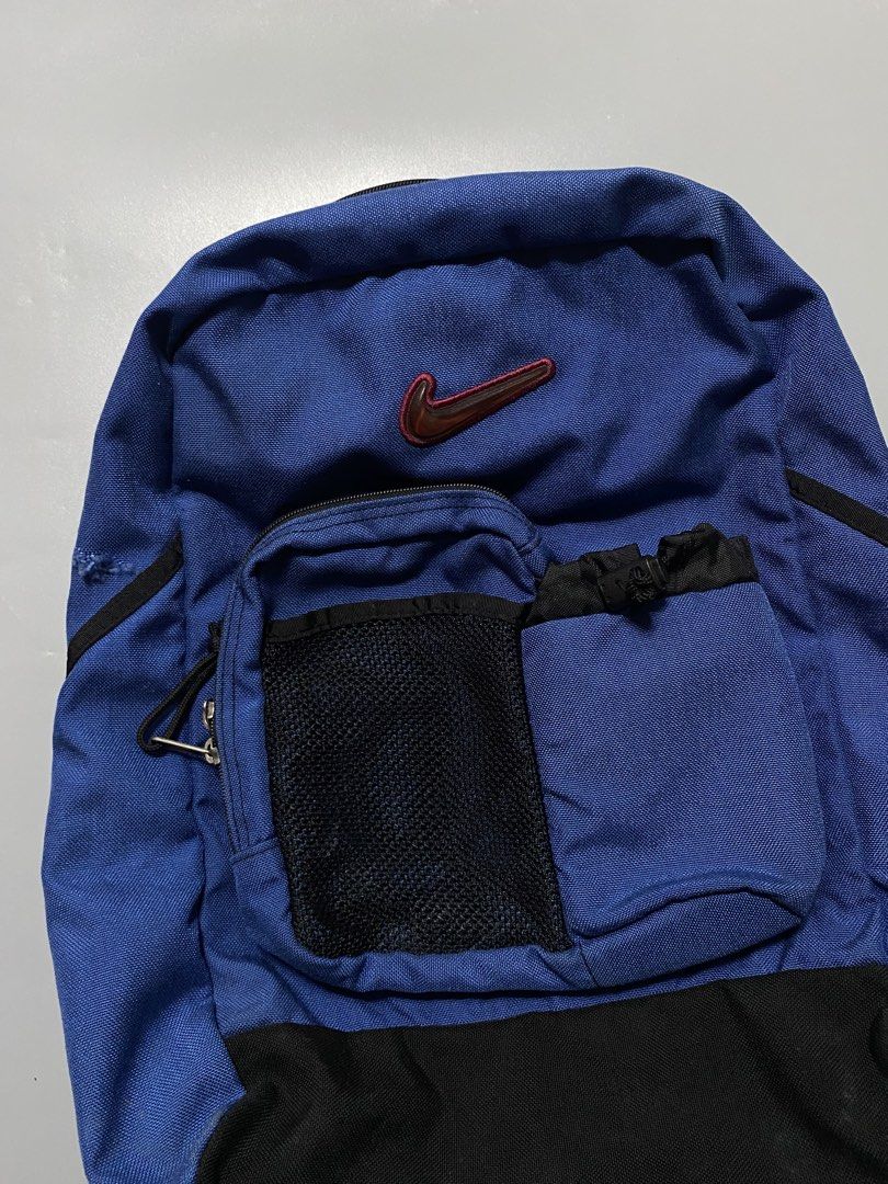 Nike Blue and Black Backpack (Category: Backpacks) located in Manila. Submitted by delunakenn94368 (Listing ID 1466695746, Image 2). Description: - Brand: Nike - Color: Blue and black with a red embroidered swoosh logo - Storage: Front mesh pocket and zippered compartment for easy organization - Durability: Black reinforced base panel for extra protection - Comfort: Adjustable shoulder straps featuring Nike branding on the buckles.