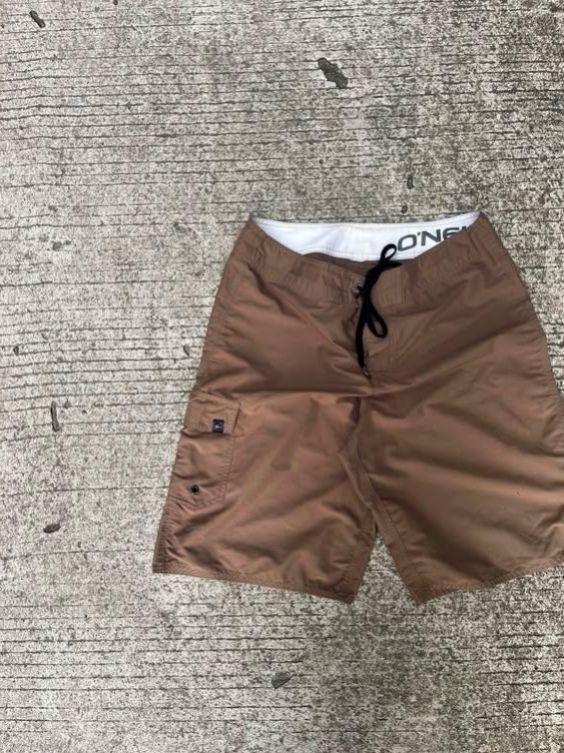 O'Neill Brown Board Shorts (Category: Swim Trunks & Board Shorts) located in Sipalay. Submitted by yon.thrifter (Listing ID 1466773437, Image 3). Description: - Brand: O'Neill - Color: Solid brown with white inner waistband and black drawstring - Material: Quick-drying fabric for all-day comfort - Pockets: Small side cargo pocket with button closure and logo tag, plus a back pocket with matching button - Fit: Standard fit - Ideal for: Beach trips