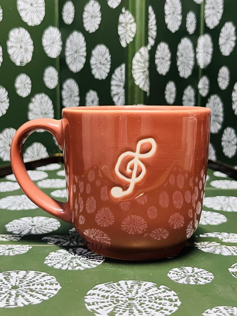 Orange Ceramic Mug with Music Note and Text (Category: Coffee & Tea Tableware) located in Malabon City. Submitted by mgsurplus (Listing ID 1466576886, Image 2). Description: - Vibrant orange ceramic mug with a glossy finish and playful polka dot pattern - Front features embossed white 'BÉBÉ JOYEUX' lettering in a circle with a music note - Reverse side showcases a stylish white treble clef design - Equipped with a comfortable handle and a sturdy 
