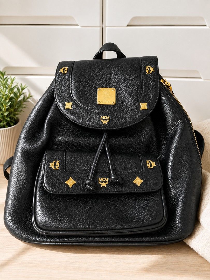 Original MCM Backpack (Category: Backpacks) located in Manila. Submitted by coolbear.5772e6 (Listing ID 1466731853, Image 1). Description: Highlights - black - leather - grained texture - gold-tone stud embellishment - foldover top - magnetic fastening - drawstring fastening - single flat top handle - two adjustable shoulder straps - front flap pocket - internal zip-fastening pocket gold-tone hardware Condition: GOOD. This previously owned and us