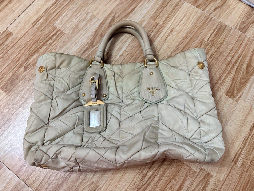 ORIGINAL Prada Quilted Nylon Tote Handbag Off White (Category: Luxury Bags & Wallets) located in Bacoor. Submitted by preownedparadyse (Listing ID 1466753887, Image 1). Description: - Brand: Prada - Style: Quilted nylon tote bag MISSING SLING - Color: light green with gold-tone hardware - Features: Dual top handles, front buckle tag, quilted pattern - Condition: Pre-loved with visible discoloration, stains, and dirt marks on the fabric and corner