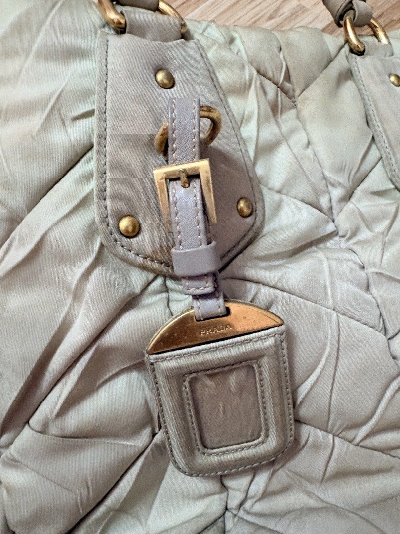 ORIGINAL Prada Quilted Nylon Tote Handbag Off White (Category: Luxury Bags & Wallets) located in Bacoor. Submitted by preownedparadyse (Listing ID 1466753887, Image 3). Description: - Brand: Prada - Style: Quilted nylon tote bag MISSING SLING - Color: light green with gold-tone hardware - Features: Dual top handles, front buckle tag, quilted pattern - Condition: Pre-loved with visible discoloration, stains, and dirt marks on the fabric and corner