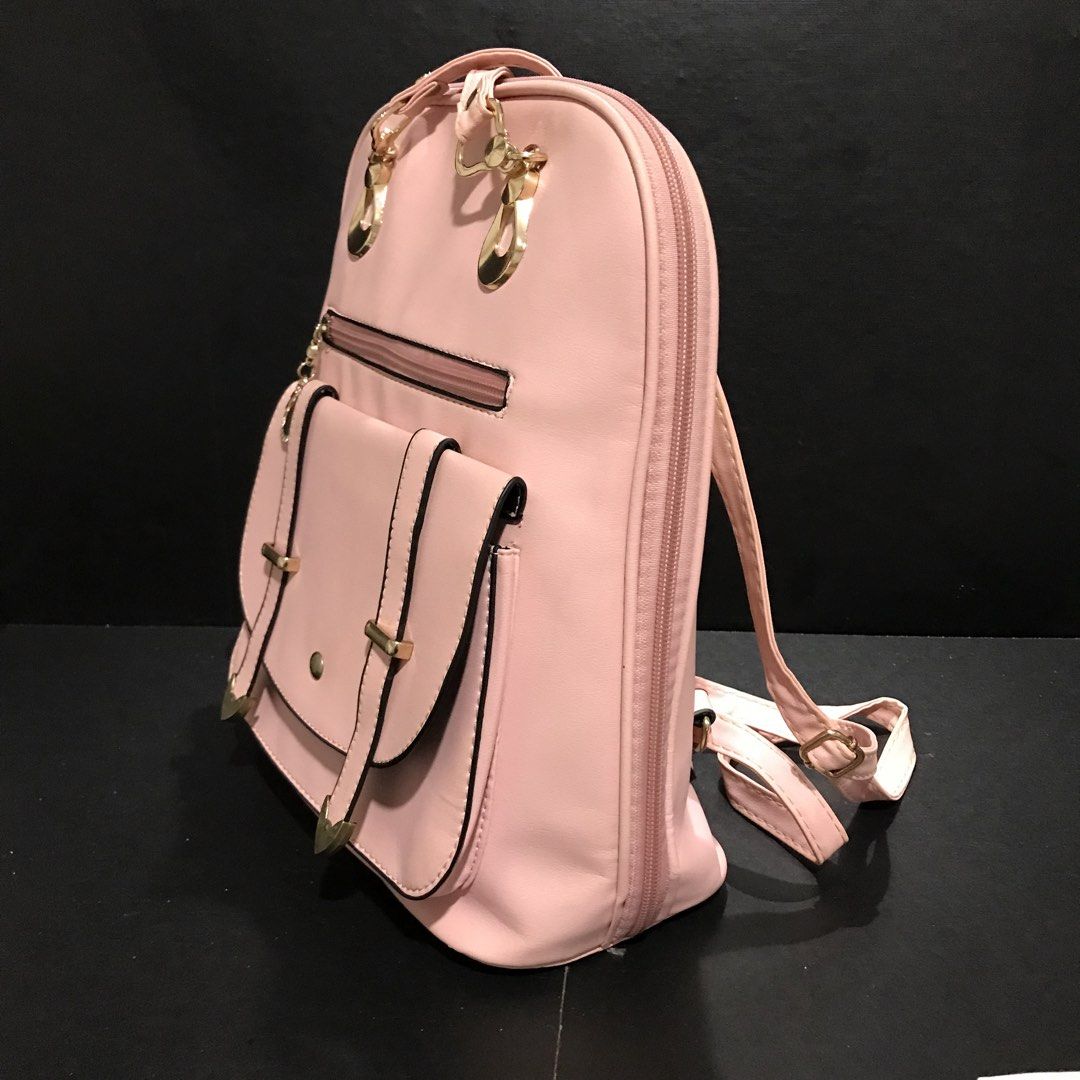 Pink faux leather backpack with gold hardware (Category: Backpacks) located in Baao. Submitted by all.things.japan (Listing ID 1466701589, Image 3). Description: - Color: Soft pink - Material: Smooth synthetic leather with polished gold-tone hardware - Pockets: Front flap pocket with magnetic snap & decorative straps, plus an extra front zippered pocket - Straps: Adjustable matching pink shoulder straps - Closure: Secure zip-around main compartme