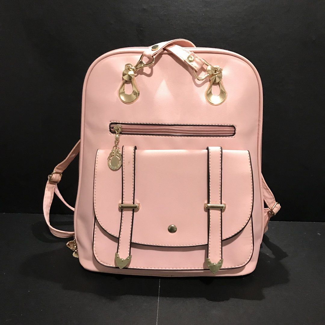 Pink faux leather backpack with gold hardware (Category: Backpacks) located in Baao. Submitted by all.things.japan (Listing ID 1466701589, Image 2). Description: - Color: Soft pink - Material: Smooth synthetic leather with polished gold-tone hardware - Pockets: Front flap pocket with magnetic snap & decorative straps, plus an extra front zippered pocket - Straps: Adjustable matching pink shoulder straps - Closure: Secure zip-around main compartme
