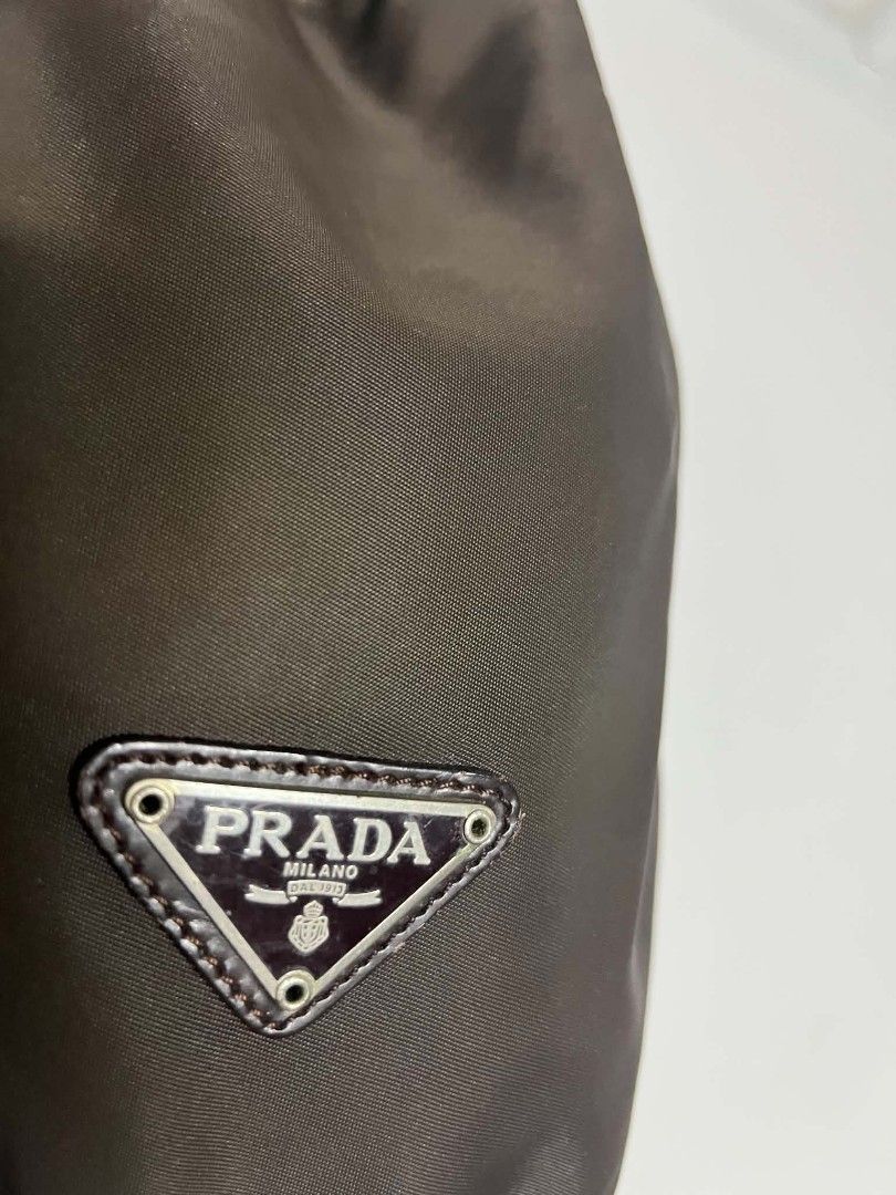 Prada Brown Nylon Bucket Bag (Category: Luxury Bags & Wallets) located in Manila. Submitted by cleverearth.125e3f (Listing ID 1466667536, Image 3). Description: - Authentic Prada nylon bucket bag in a classic brown shade - Made in Italy with durable fabric and silver-tone hardware - Drawstring closure with a secure leather pull - Features the iconic triangular metal logo plaque on the front - Compact and versatile design for shoulder or hand carr
