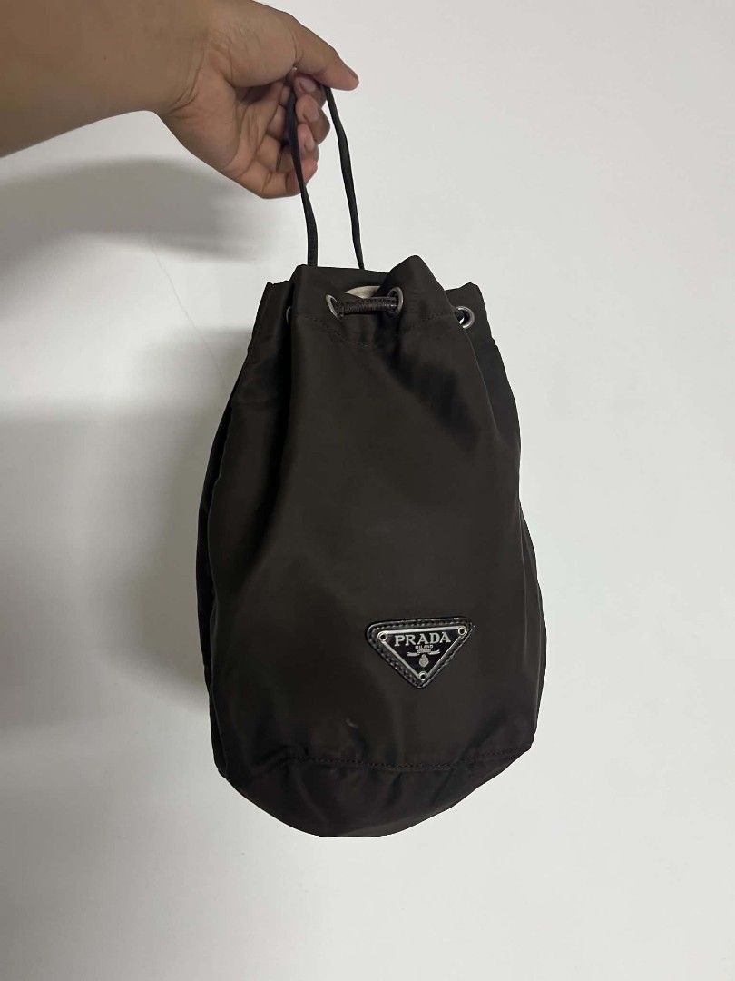 Prada Brown Nylon Bucket Bag (Category: Luxury Bags & Wallets) located in Manila. Submitted by cleverearth.125e3f (Listing ID 1466667536, Image 1). Description: - Authentic Prada nylon bucket bag in a classic brown shade - Made in Italy with durable fabric and silver-tone hardware - Drawstring closure with a secure leather pull - Features the iconic triangular metal logo plaque on the front - Compact and versatile design for shoulder or hand carr
