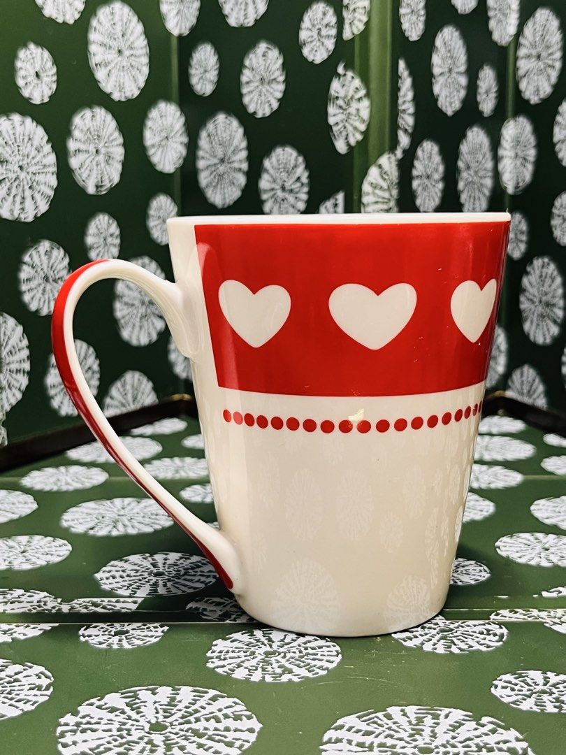 Red and White Ceramic Coffee Mug with Heart Pattern (Category: Coffee & Tea Tableware) located in Malabon City. Submitted by mgsurplus (Listing ID 1466577048, Image 2). Description: - Material: Sturdy ceramic - Design: Bold red top with white hearts, off-white floral lower section, and red polka dot separator - Handle: Matching handle featuring a stylish red stripe - Capacity: Holds standard hot beverages - Condition: Brand new / Excellent - Mode