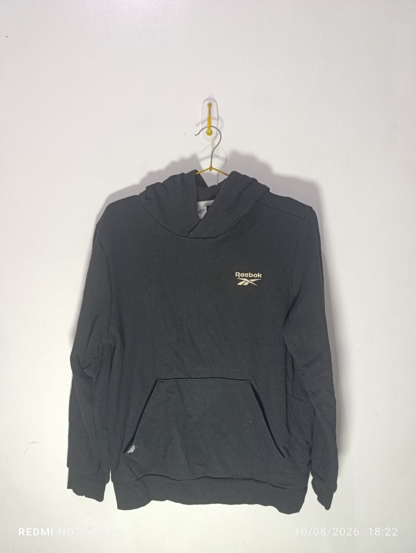 Reebok Black Hoodie Pullover (Category: Coats, Jackets and Outerwear) located in Pasig City. Submitted by firstpick_thrift (Listing ID 1466772343, Image 2). Description: - Brand: Reebok - Color: Black - Style: Classic pullover hoodie with front pocket - Details: Small logo on front chest, crossover hood design - Fit: Snug ribbed cuffs and hem - Material: Soft and comfortable fabric, perfect for daily wear - Easy to pair with jeans or sweatpants.