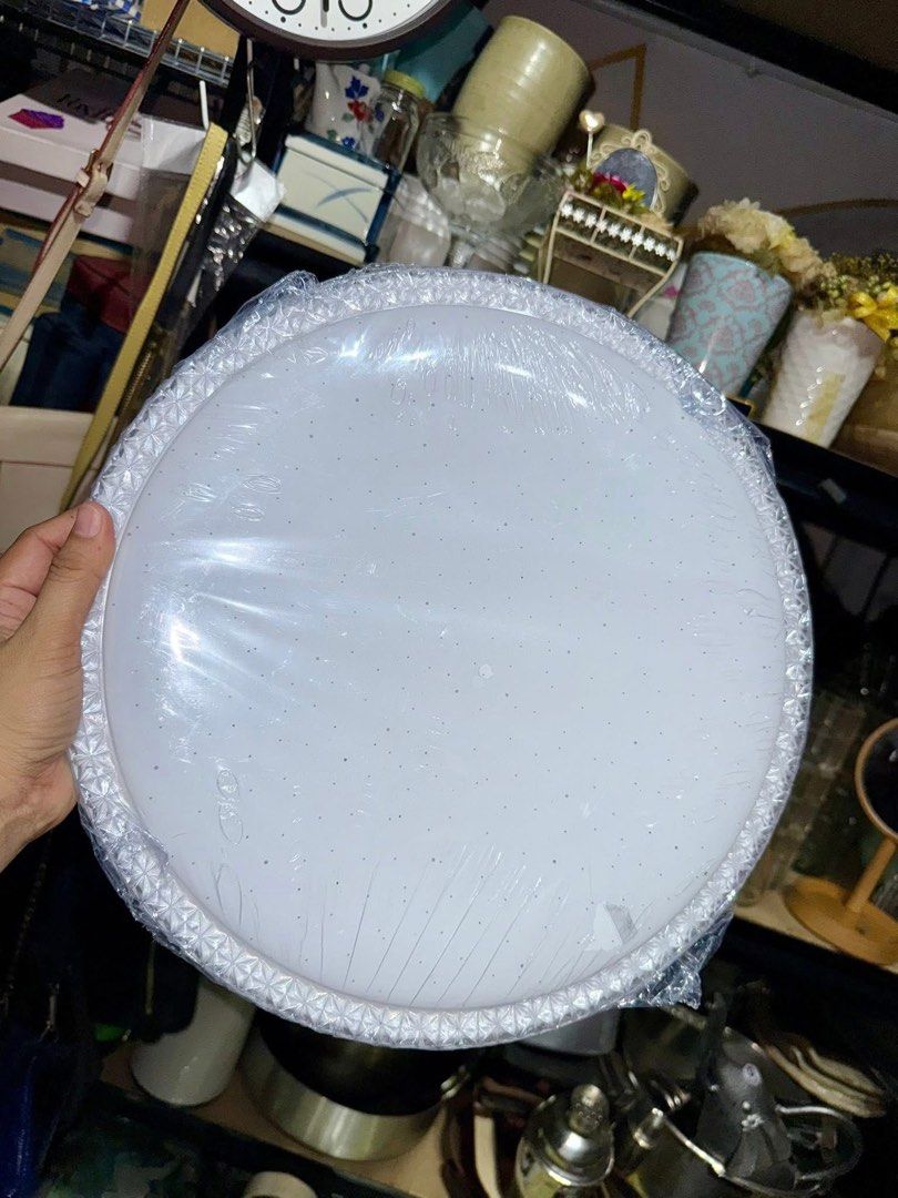 Round LED Ceiling Light White Fixture (Category: Lighting) located in Pilar. Submitted by faveanyshop (Listing ID 1466578646, Image 2). Description: - Type: Round white flush mount ceiling light fixture - Design: Decorative edge pattern with a subtle starry dot cover - Condition: Brand new, still wrapped in original protective plastic - Installation: Metal backing plate with pre-drilled holes and exposed wires for easy hardwiring - Finish: Clean 