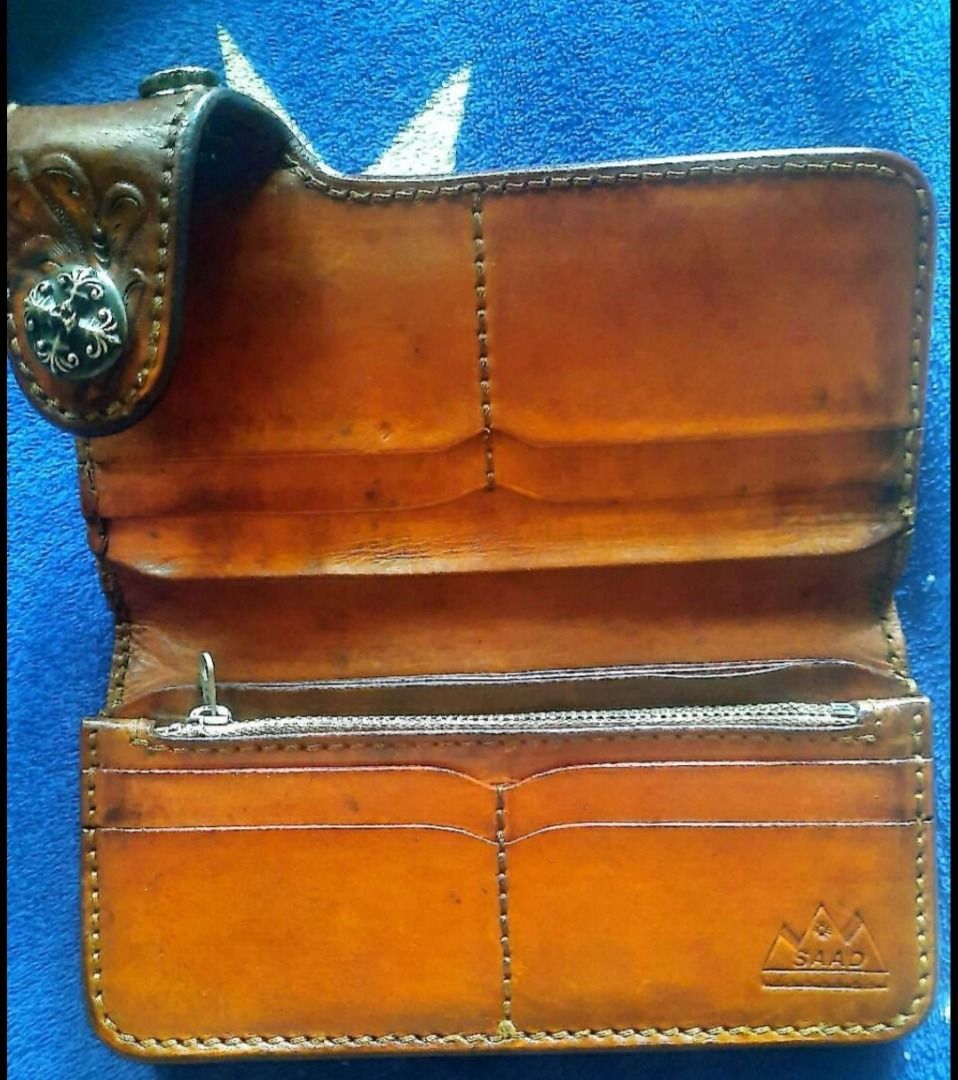 SAAD Leather Long Wallet Tooled Design (Category: Wallets & Card holders) located in Santa Cruz. Submitted by freeturtle_2610 (Listing ID 1466764490, Image 2). Description: - Brand: SAAD - Material: Genuine leather in tan brown - Exterior: Hand-tooled floral carved pattern with a snap button closure and decorative metal concho - Interior: Multiple card slots, spacious bill compartments, and a zippered coin pocket - Details: Stamped with the SAAD 