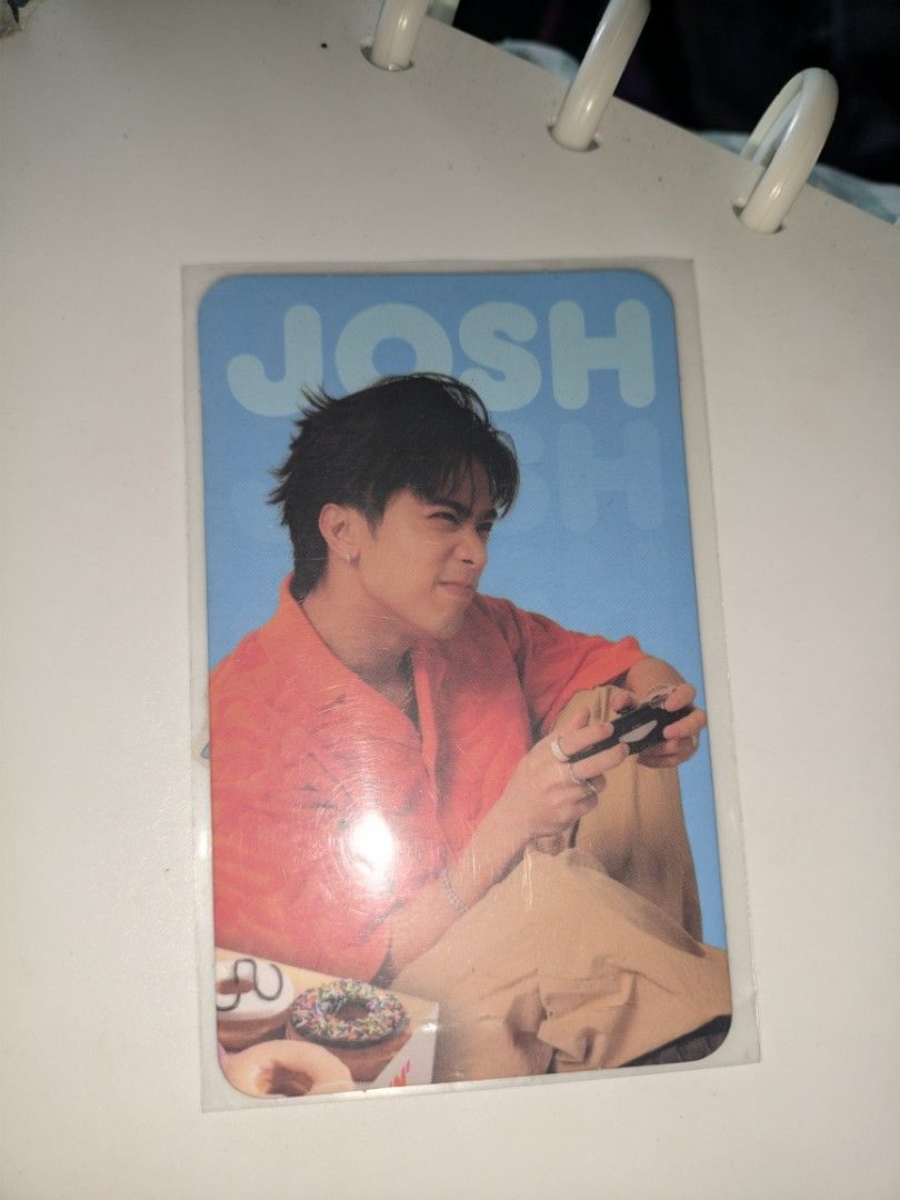SB19 Josh Dunkin Photocard (Category: K-Wave Merchandise) located in Manila. Submitted by silenthawk_b2544d (Listing ID 1466599736, Image 1). Description: - Official SB19 x Dunkin collaboration photocard - Variant: Josh (Blue background, orange shirt, holding a game controller) - Back design: SB19 logo, Dunkin branding, and Josh's gamer fun fact - Size: Standard photocard size with rounded corners - Condition: Mint, kept in a clear sleeve for pro