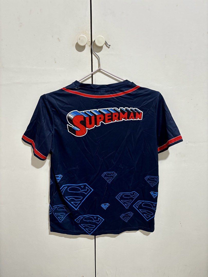 Shein Superman Baseball T-Shirt Size (Category: Shirts) located in Manila. Submitted by dianafayesimbre (Listing ID 1466770261, Image 3). Description: - Size: 11 Years old but can fit xxs to medium womens - Unisex - Design: Dark blue Superman baseball jersey style with red piping - Details: Bold 3D-effect logo on chest and back, plus a yellow and red chest shield - Accent: Subtle blue Superman emblem patterns near the bottom hem - Material: Smoot
