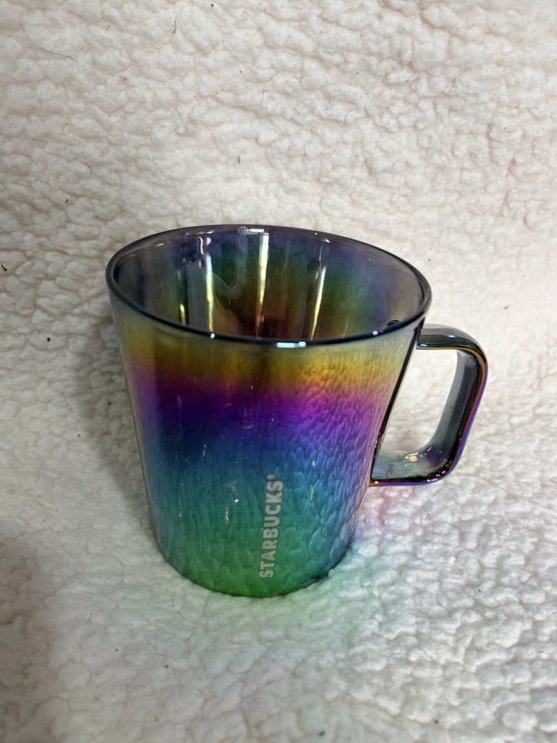 Starbucks Iridescent Rainbow Coffee Mug (Category: Coffee & Tea Tableware) located in Makati City. Submitted by starbeans888 (Listing ID 1466693234, Image 2). Description: Starbucks ceramic mug with an oil slick rainbow finish. Glossy surface catches the light differently from every angle. White Starbucks lettering printed on the side. Geometric paneling around the base on one design and a smooth finish on the other. Comfortable squared handle. G