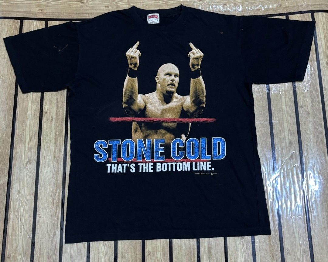 Stone Cold Tshirt (Category: Activewear) located in Santo Tomas. Submitted by rency_thrift (Listing ID 1466673172, Image 1). Description: The image shows a black vintage-style Stone Cold Steve Austin WWF Graphic T-Shirt featuring a photo of "Stone Cold" Steve Austin raising both middle fingers behind a red ring rope, with the bold blue text "STONE COLD" and the signature quote "THAT'S THE BOTTOM LINE." Dimes: 23.5 × 29.5 Size: XL on tag.