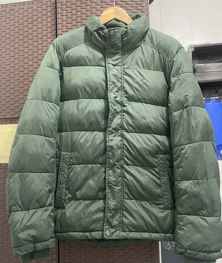 Tommy Hilfiger Green Puffer Jacket (Category: Coats, Jackets and Outerwear) located in Manila. Submitted by oenthrift.2026 (Listing ID 1466709141, Image 1). Description: - Brand: Tommy Hilfiger - Color: Olive green with bright orange inner lining - Design: High collar with ribbed inner lining, full zip and snap button closure - Details: Iconic embroidered flag logo on the left chest - Pockets: Two functional front slash pockets - Warmth: Heavy qu