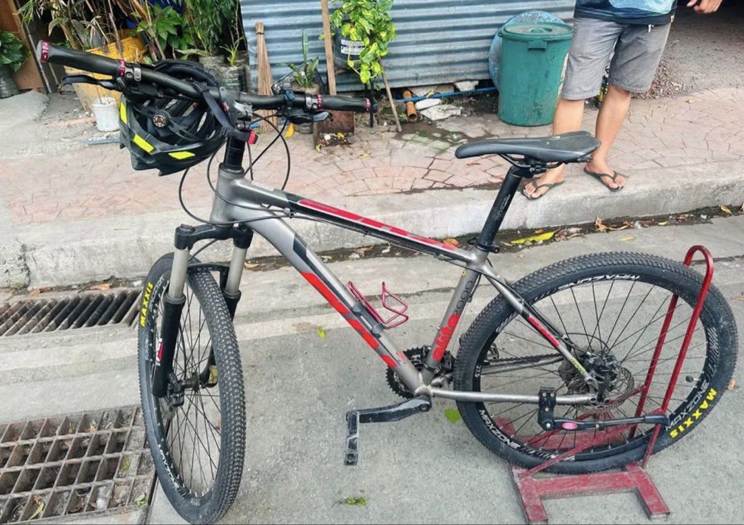 Trinx Elite 2000 Mountain Bike (Category: Bicycles) located in Manila. Submitted by frim06 (Listing ID 1466664509, Image 1). Description: - Brand/Model: Trinx Elite 2000 Mountain Bike - Color: Grey and Red frame - Tires: 27.5-inch Maxxis tires - Suspension: Front suspension fork setup - Included Accessories: Mounted bottle cage, flat pedals, and a black helmet on the left grip - Condition: Frame shows standard use marks.