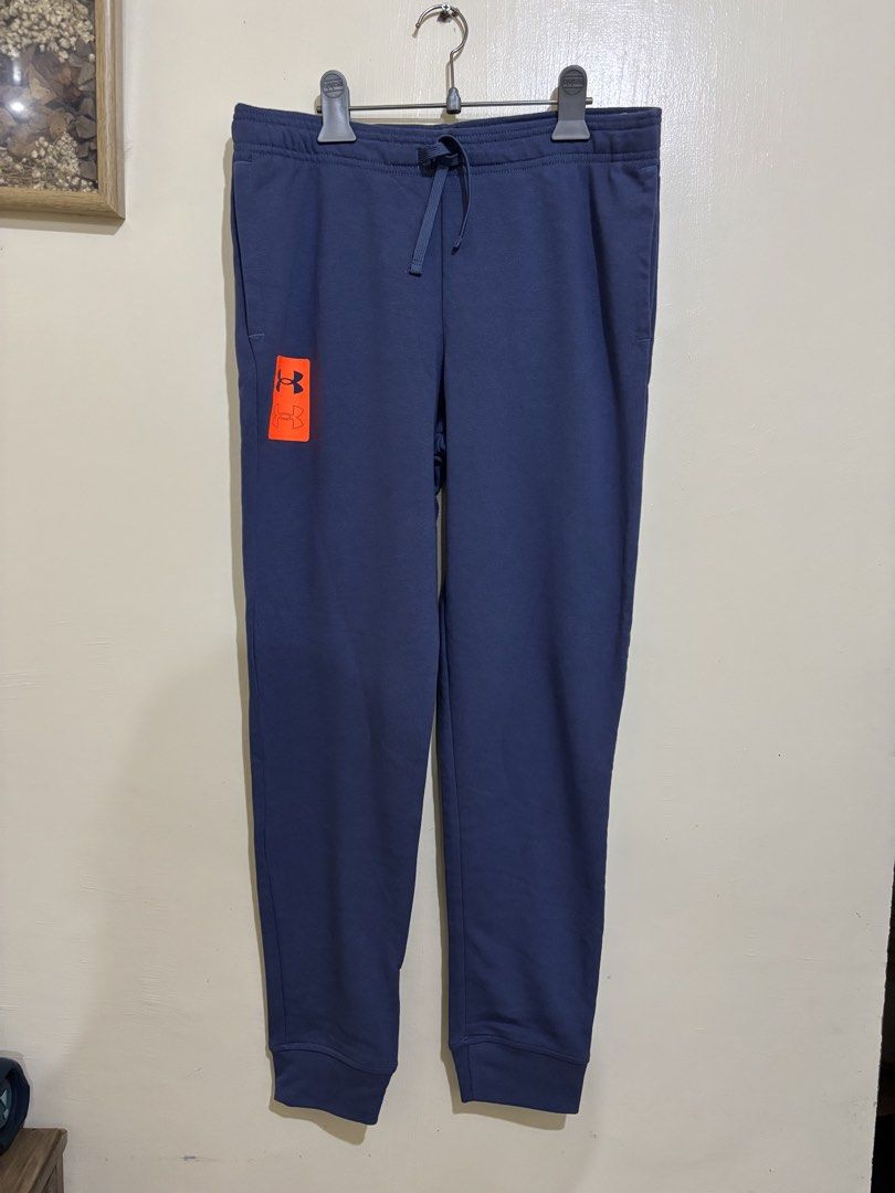 Under Armour Blue Joggers Sweatpants (Category: Joggers) located in Balayan. Submitted by authenticfindsbymrb (Listing ID 1466702462, Image 1). Description: - Brand/Item: Blue Under Armour sweatpants - Fit: Standard fit with adjustable drawstring waist and cuffed ankles - Design: Bright orange logo graphic on the right leg - Pockets: Two deep side pockets with mesh lining - Material: Soft cotton blend with cozy French terry inner lining - Use: Id