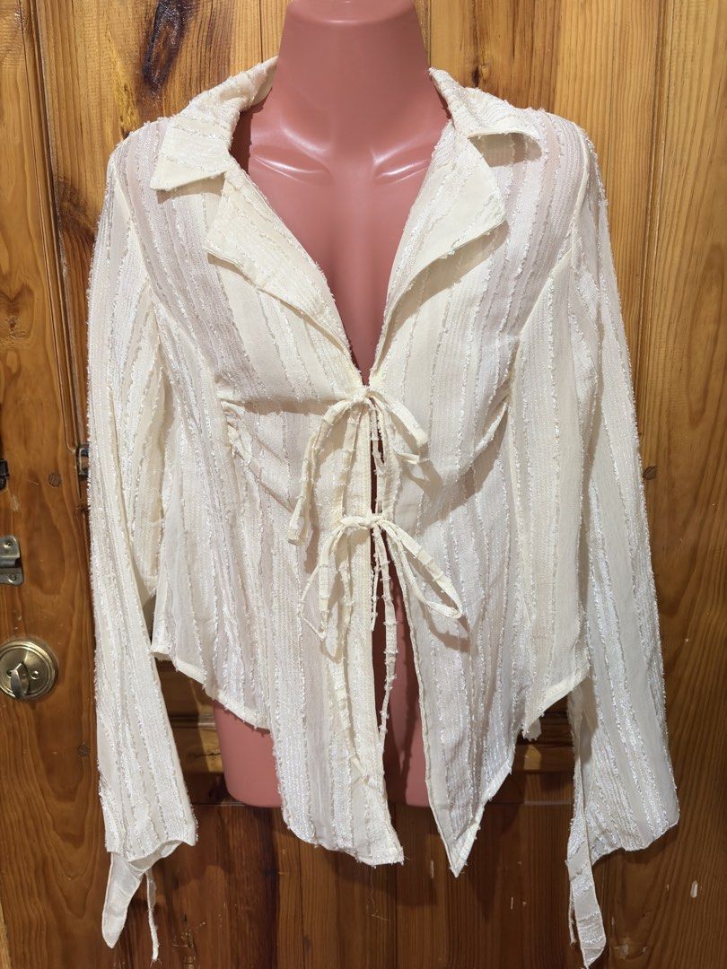 White textured tie-front long sleeve blouse (Category: Blouses) located in Baguio. Submitted by declutterbycys (Listing ID 1466569252, Image 2). Description: - Color: Cream white - Design: Textured vertical stripes with open V-neck collar and double front tie closures - Fit: Lightweight, sheer, and flowy draped fit - Sleeves: Long sleeves with stylish flared cuffs - Styling: Versatile neutral piece, great to pair with denim or skirts.