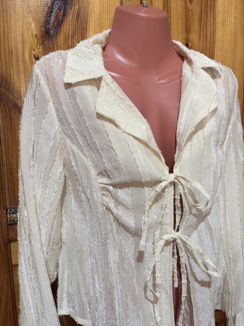 White textured tie-front long sleeve blouse (Category: Blouses) located in Baguio. Submitted by declutterbycys (Listing ID 1466569252, Image 3). Description: - Color: Cream white - Design: Textured vertical stripes with open V-neck collar and double front tie closures - Fit: Lightweight, sheer, and flowy draped fit - Sleeves: Long sleeves with stylish flared cuffs - Styling: Versatile neutral piece, great to pair with denim or skirts.