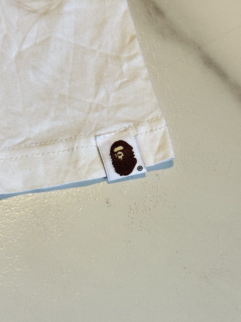 A Bathing Ape Bape Camo Logo Tee White XXL (Category: Tshirts & Polo Shirts ) located in Cavite. Submitted by remcadzzz (Listing ID 1466895424, Image 3). Description: - Brand: A Bathing Ape (Bape) - Color: White - Size: XXL (Tag at collar) - Design: Classic camo ape head logo with 'A Bathing Ape World Gone Mad 1993 to 2093' text - Details: Signature sleeve tag on the left arm, crew neck cut - Condition: Clean fabric, great for everyday streetwear