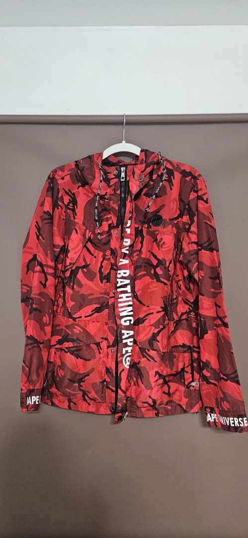Aape By A Bathing Ape Red Camo Jacket Size L (Category: Coats, Jackets and Outerwear) located in Santa Maria. Submitted by rommelmateo (Listing ID 1466935231, Image 1). Description: - Brand: Aape by A Bathing Ape - Style: Red camo windbreaker jacket - Size: Large (with signature Aape neck tag) - Details: Bold graphic text on front placket, 'AAPE UNIVERSE' lettering on sleeves - Features: Multiple front utility pockets with zip closures and black 