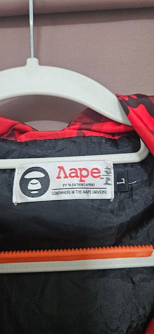 Aape By A Bathing Ape Red Camo Jacket Size L (Category: Coats, Jackets and Outerwear) located in Santa Maria. Submitted by rommelmateo (Listing ID 1466935231, Image 3). Description: - Brand: Aape by A Bathing Ape - Style: Red camo windbreaker jacket - Size: Large (with signature Aape neck tag) - Details: Bold graphic text on front placket, 'AAPE UNIVERSE' lettering on sleeves - Features: Multiple front utility pockets with zip closures and black 