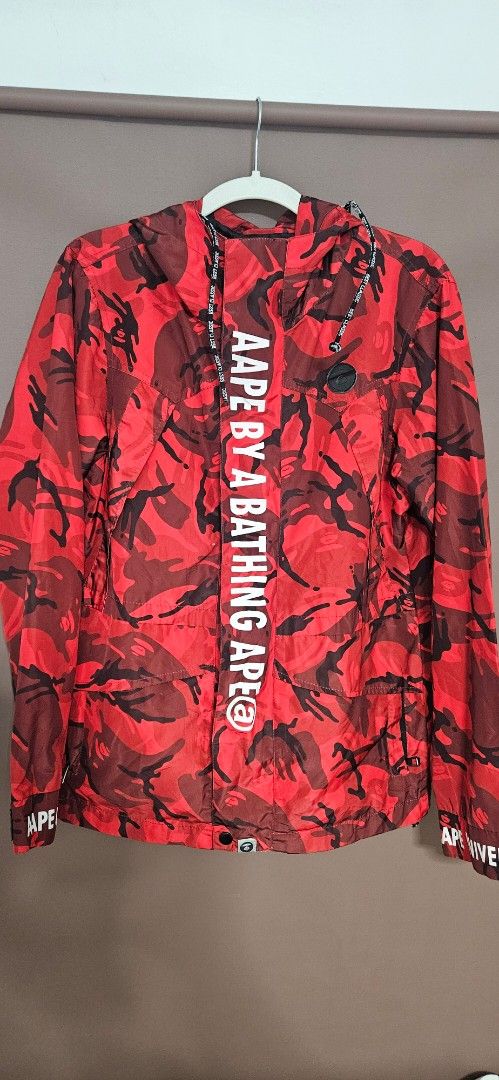 Aape By A Bathing Ape Red Camo Jacket Size L (Category: Coats, Jackets and Outerwear) located in Santa Maria. Submitted by rommelmateo (Listing ID 1466935231, Image 2). Description: - Brand: Aape by A Bathing Ape - Style: Red camo windbreaker jacket - Size: Large (with signature Aape neck tag) - Details: Bold graphic text on front placket, 'AAPE UNIVERSE' lettering on sleeves - Features: Multiple front utility pockets with zip closures and black 