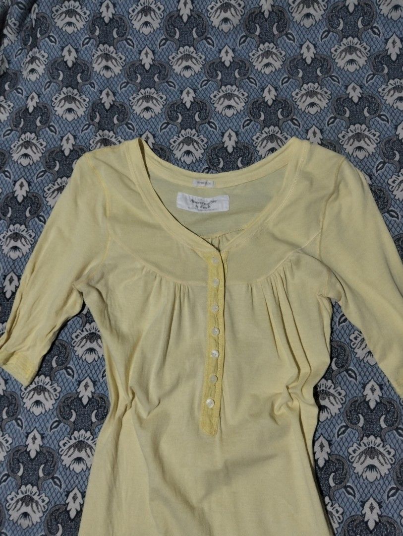 Abercrombie & Fitch Stretch Yellow Button-Front Top (Category: Blouses) located in Sibulan. Submitted by paulbrain (Listing ID 1466906619, Image 2). Description: - Brand: Abercrombie & Fitch - Size: Medium Width 15 x Length 26.6 - Color: Vibrant Yellow - Material: 90% Cotton, 10% Elastane (Stretch blend) - Design: Button-front placket, scoop neckline, and 3/4 sleeves - Detail: Signature embroidered moose logo near the bottom hem - Origin: Made in