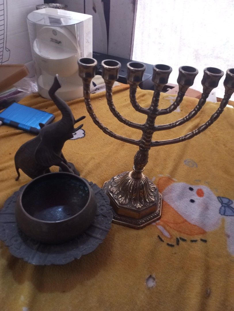 Antique collections (Category: Vintage Collectibles) located in Manila. Submitted by buknoybuknay (Listing ID 1466873190, Image 1). Description: Seven-Branched Menorah: The prominent brass candelabra on the right with seven candle holders arranged symmetrically. It is a traditional symbol in Judaism representing the ancient candelabra used in the Temple. Metal Elephant Figurine: A small brass or bronze statuette of an elephant with its trunk rais