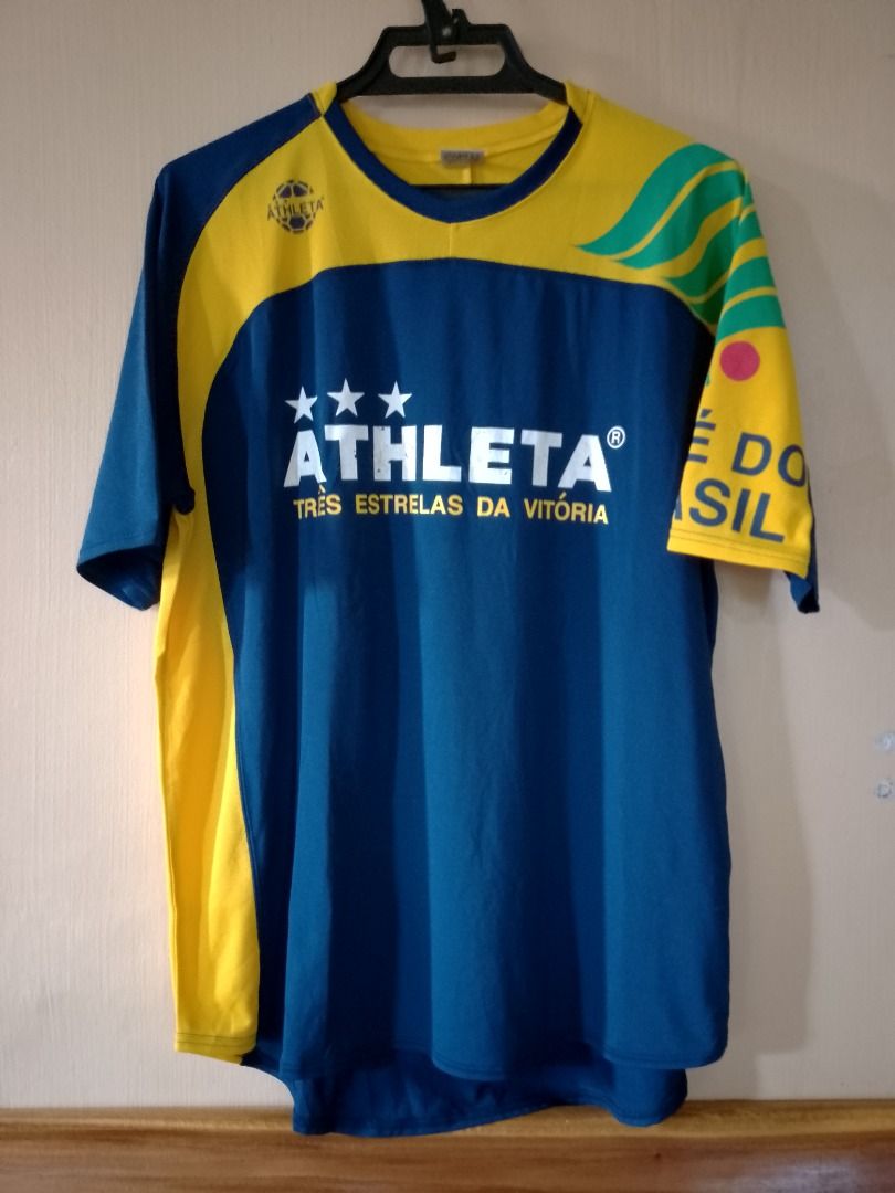Athleta Três Estrelas Da Vitória Jersey (Category: Activewear) located in Bayombong. Submitted by daily10 (Listing ID 1466875906, Image 2). Description: - Est Size: O (XL) - Dimensions: 23" x 29f" x 31b" - Authentic Athleta soccer jersey in classic blue with striking yellow and green accents - Features bold 'ATHLETA' and 'TRÊS ESTRELAS DA VITÓRIA' chest branding - Detailed with 'CAFE DO BRASIL' text and green wave graphics on the sleeves - Comfor