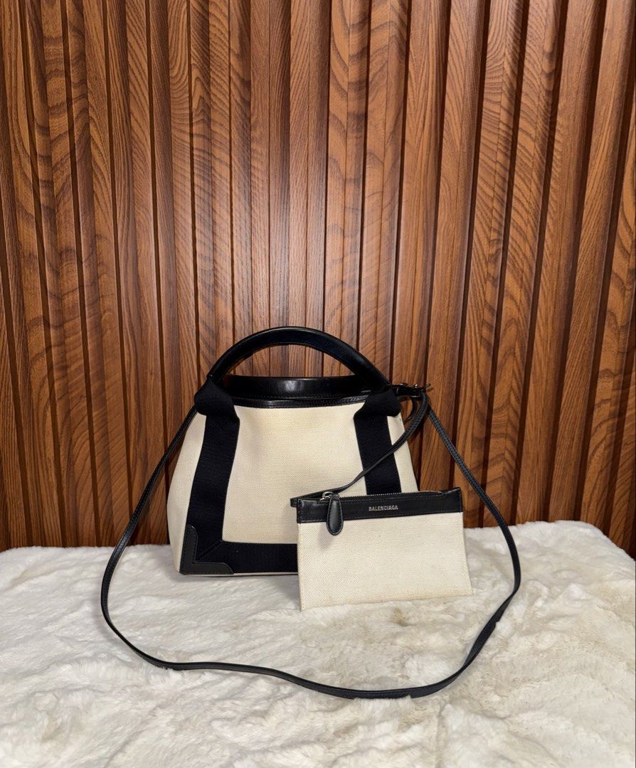 Authentic Balenciaga Navy Cabas Canvas Tote Bag (Category: Tote Bags) located in Subic. Submitted by luxshoppe88 (Listing ID 1466876458, Image 2). Description: - Authentic Balenciaga Navy Cabas Tote - Color: Cream canvas with black leather trim - Includes detachable matching zippered pouch - Dual top handles and long shoulder strap - Black interior lining with leather brand patch - Condition: Minor wear and scuffs on the base, with some faint dis