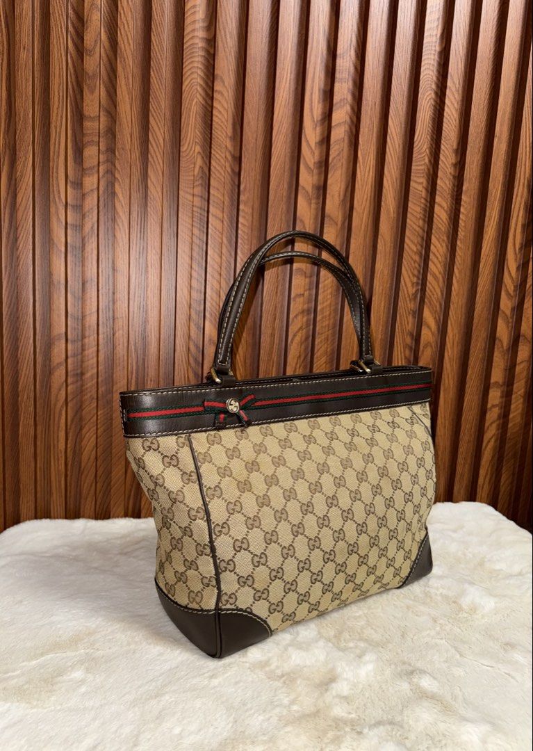 Authentic Gucci GG Canvas Web Stripe Tote Bag Brown (Category: Tote Bags) located in Subic. Submitted by luxshoppe88 (Listing ID 1466874380, Image 2). Description: Authentic classic Gucci tote in beige and ebony GG canvas with dark brown leather trim, signature red and green web stripe, and a charming gold-toned bow. Features dual shoulder straps, magnetic snap closure, and a spacious cream fabric interior with a zip pocket. Made in Italy. A time