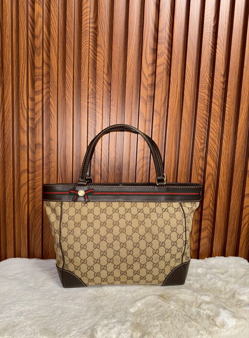 Authentic Gucci GG Canvas Web Stripe Tote Bag Brown (Category: Tote Bags) located in Subic. Submitted by luxshoppe88 (Listing ID 1466874380, Image 1). Description: Authentic classic Gucci tote in beige and ebony GG canvas with dark brown leather trim, signature red and green web stripe, and a charming gold-toned bow. Features dual shoulder straps, magnetic snap closure, and a spacious cream fabric interior with a zip pocket. Made in Italy. A time