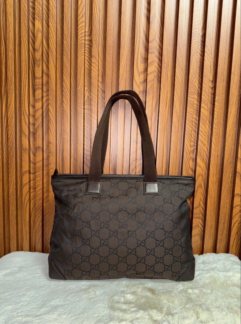Authentic Gucci GG Monogram Brown Nylon Tote Bag (Category: Luxury Bags & Wallets) located in Subic. Submitted by luxshoppe88 (Listing ID 1466874824, Image 3). Description: - Brand: Gucci - Style: GG Monogram Tote Bag - Color: Brown with dark brown leather details - Material: Durable GG monogram nylon with leather trim - Storage: Spacious main compartment and convenient front zip pocket - Straps: Sturdy brown canvas shoulder straps - Condition: C