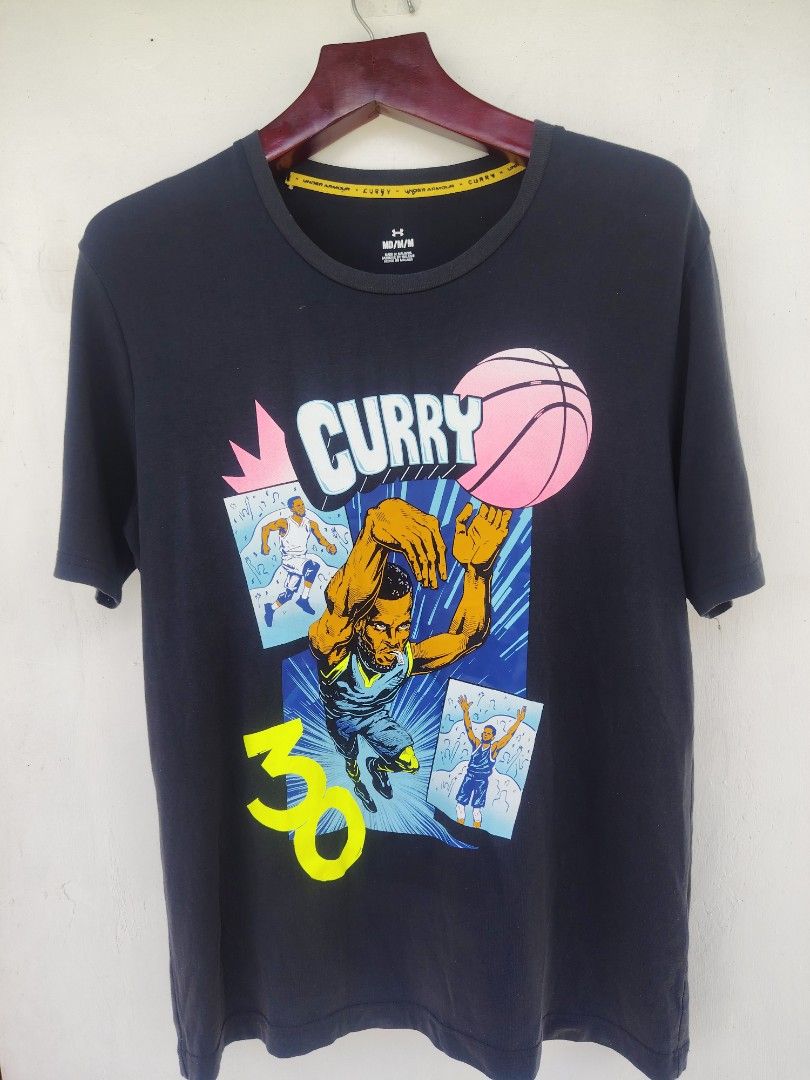 Authentic Under Armour Curry Brand "Comic Book" Graphic Tee (22x29) (Category: Tshirts & Polo Shirts ) located in Pandi. Submitted by thriftcircuit (Listing ID 1466556316, Image 1). Description: 🏀 AUTHENTIC UNDER ARMOUR CURRY BRAND "COMIC BOOK" TEE 🏀 100% Authentic Stephen Curry Brand x Under Armour short-sleeve graphic tee featuring pop-art comic illustrations of Steph shooting, his signature #30, and pink basketball accents. Details: • Brand: